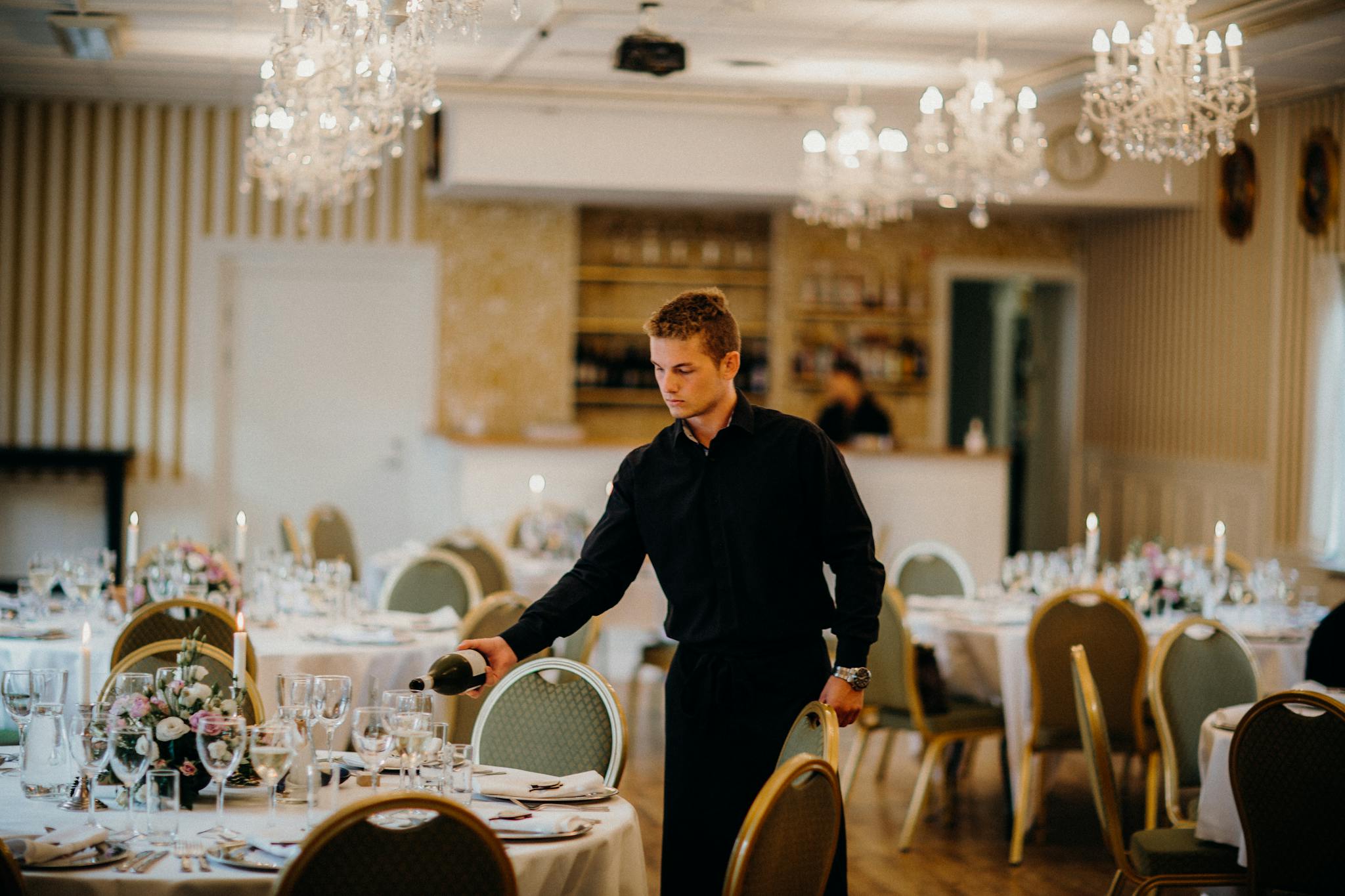 A waiter pours wine in a beautifully set dining room, creating an elegant atmosphere.